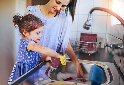 Buy stock photo Shot of a happy little girl and her mother washing the dishes together at home