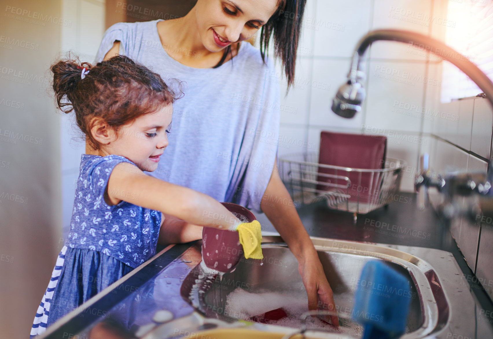 Buy stock photo Shot of a happy little girl and her mother washing the dishes together at home