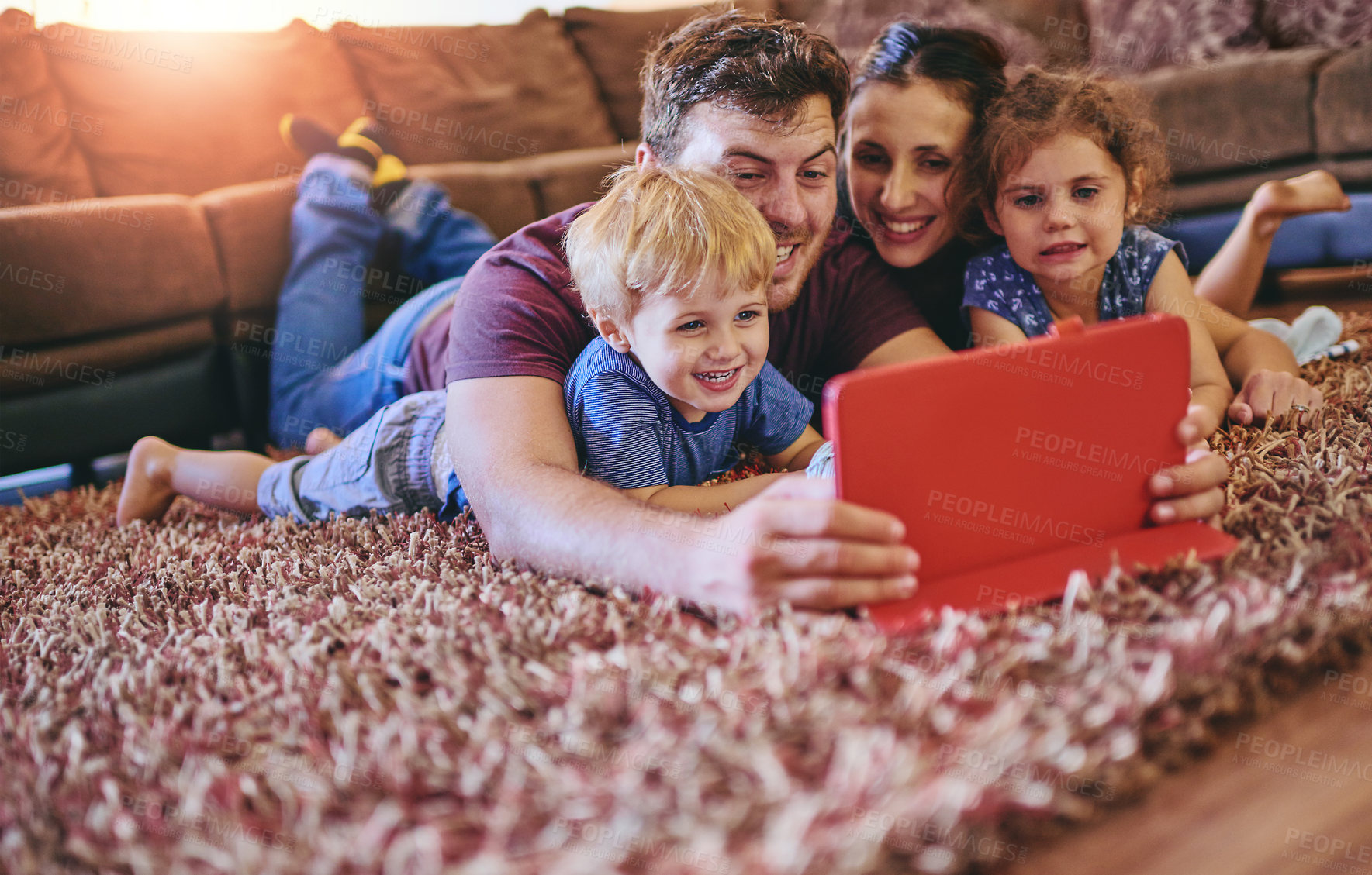 Buy stock photo Shot of a happy young family looking at a tablet together while lying on the carpet in their lounge