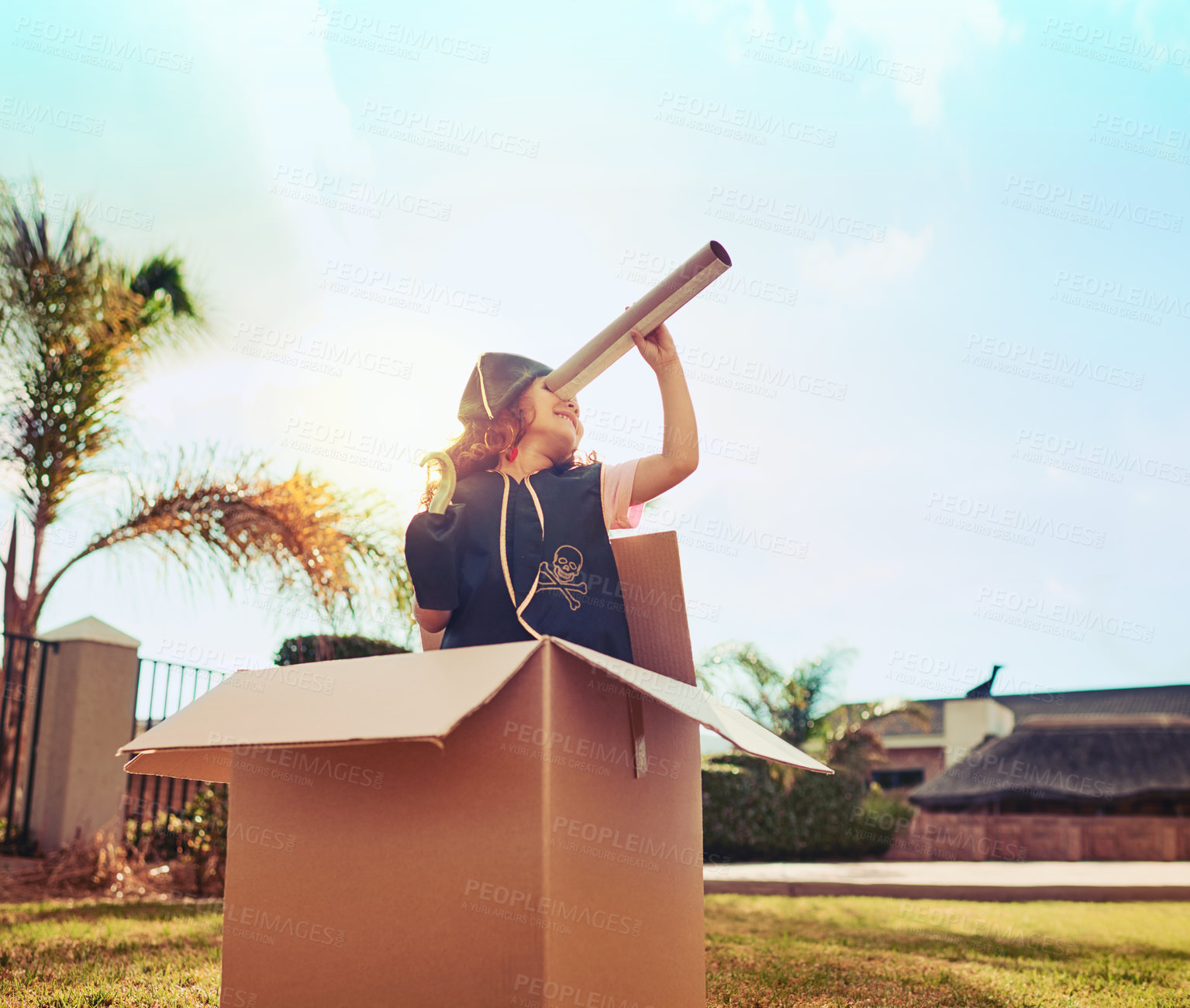 Buy stock photo Shot of a cute little girl in a pirate costume playing in a cardboard box in her backyard