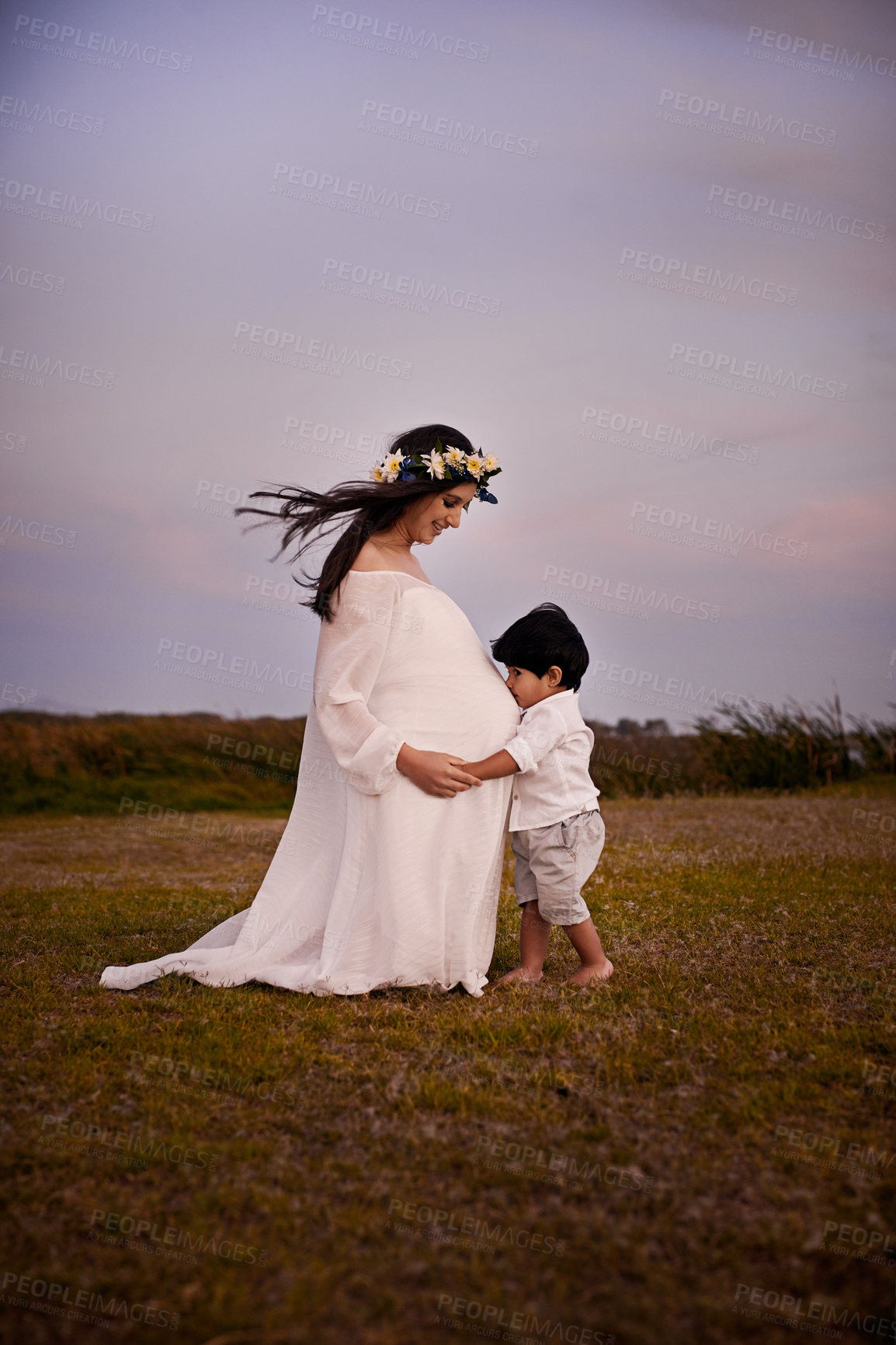 Buy stock photo Pregnant, mother and child with kiss on stomach for future sibling, love and bonding in nature. Happy, family and son by belly of woman on grass field at sunset for connection, innocence and care