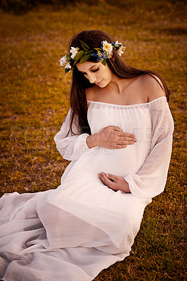 Buy stock photo Shot of a young pregnant woman holding her belly while sitting on the ground outside