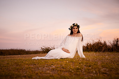 Buy stock photo Shot of a young pregnant woman holding her belly while sitting on the ground outdoors