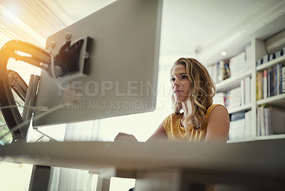 Buy stock photo Low angle shot of a young woman working on a computer in her home office