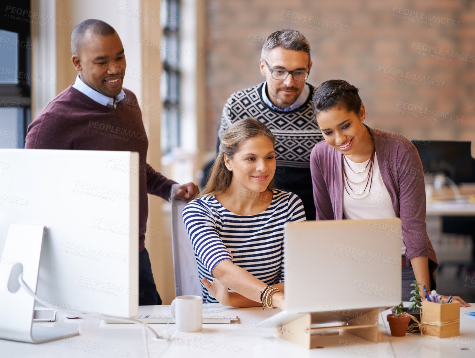 Buy stock photo Shot of a group of work colleagues in the office meeting around a laptop to point out ideas they like