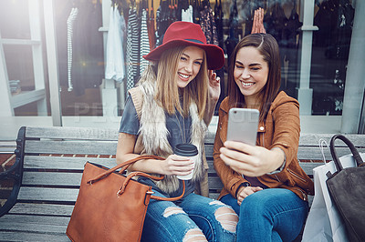 Buy stock photo Cropped shot of two young girlfriends snapping selfies while sitting on a bench during a shopping spree
