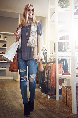 Buy stock photo Shot of a young woman walking though a boutique with a shopping bag