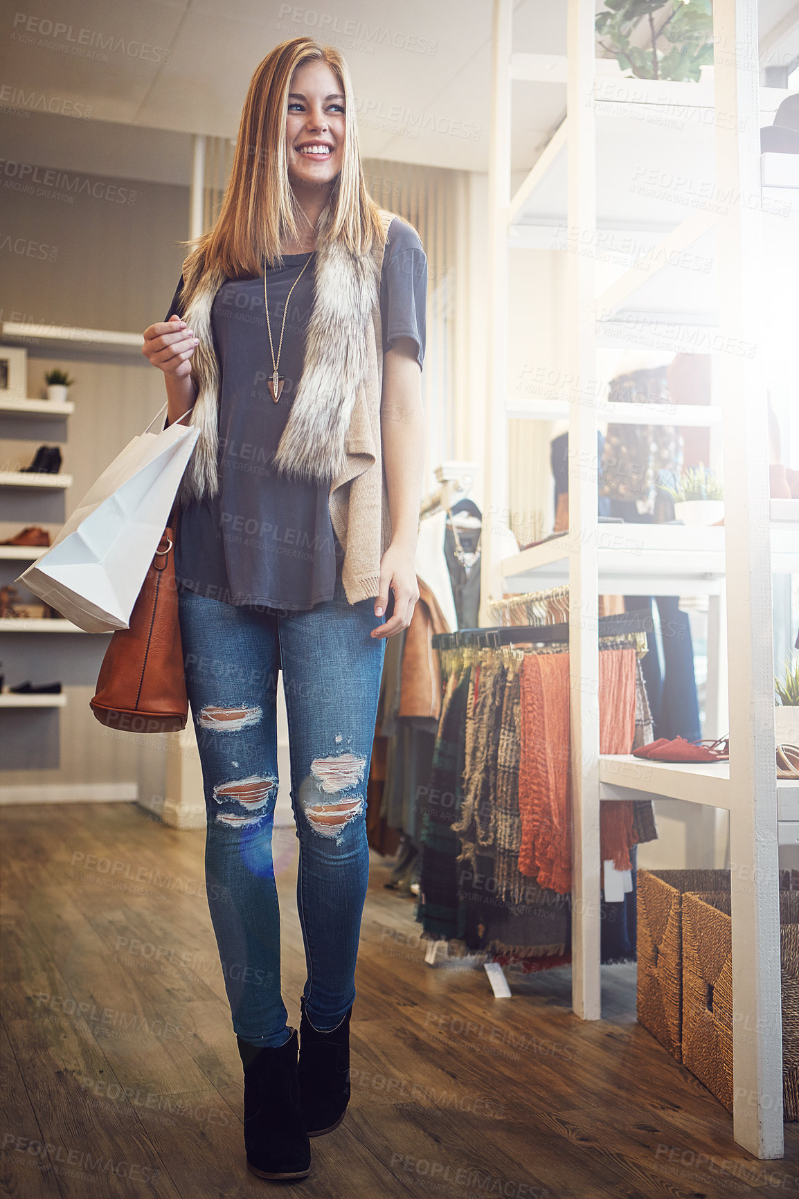 Buy stock photo Shot of a young woman walking though a boutique with a shopping bag