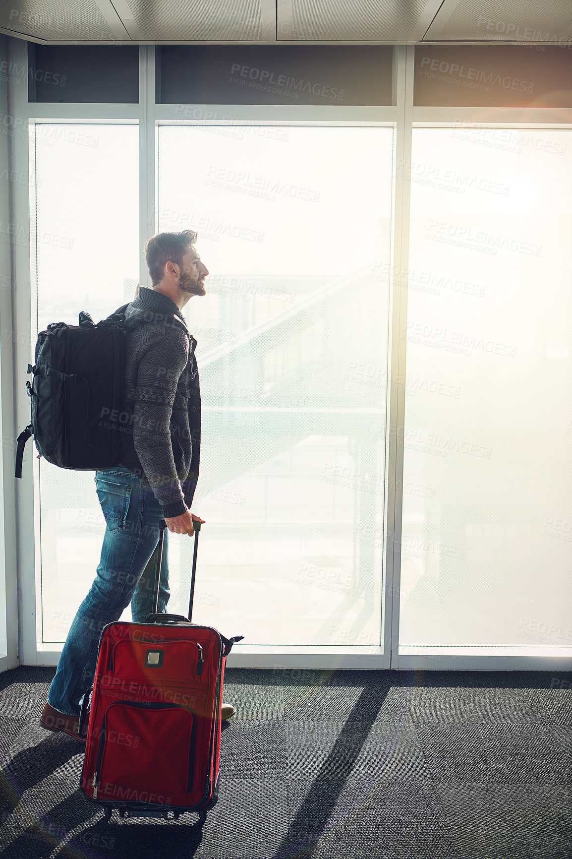 Buy stock photo Shot of a young man standing in an airport with luggage and looking at someone or something in front of him