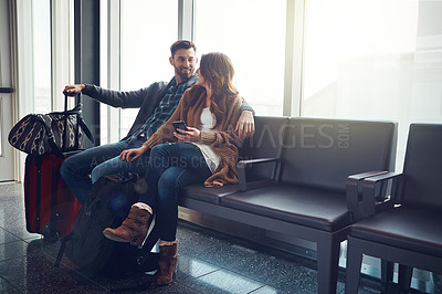 Buy stock photo Shot of a young couple seated in an airport with their luggage looking at one another and smiling