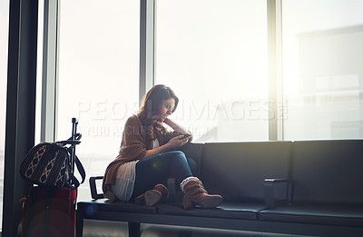 Buy stock photo Shot of a young woman sitting in an airport with her luggage and looking at her cellphone and texting someone