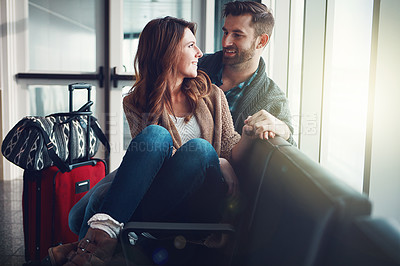 Buy stock photo Shot of a young couple sitting in an airport with their luggage and holding one another and looking at each other