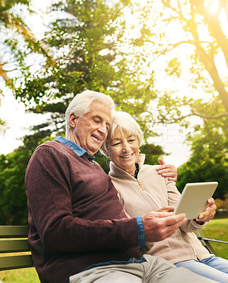 Buy stock photo Shot of a happy senior couple using a digital tablet together in the park