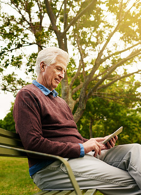 Buy stock photo Shot of a senior man sitting on a park bench and using a digital tablet