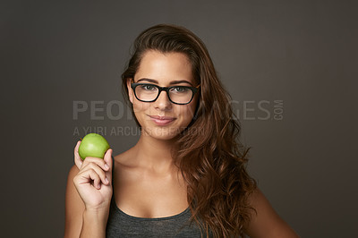 Buy stock photo Studio shot of a beautiful young woman holding an apple against a brown background