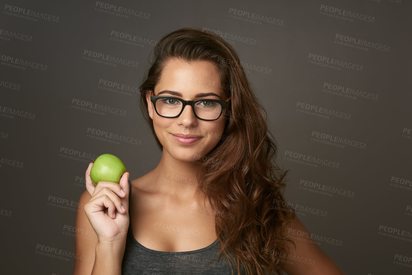 Buy stock photo Studio shot of a beautiful young woman holding an apple against a brown background
