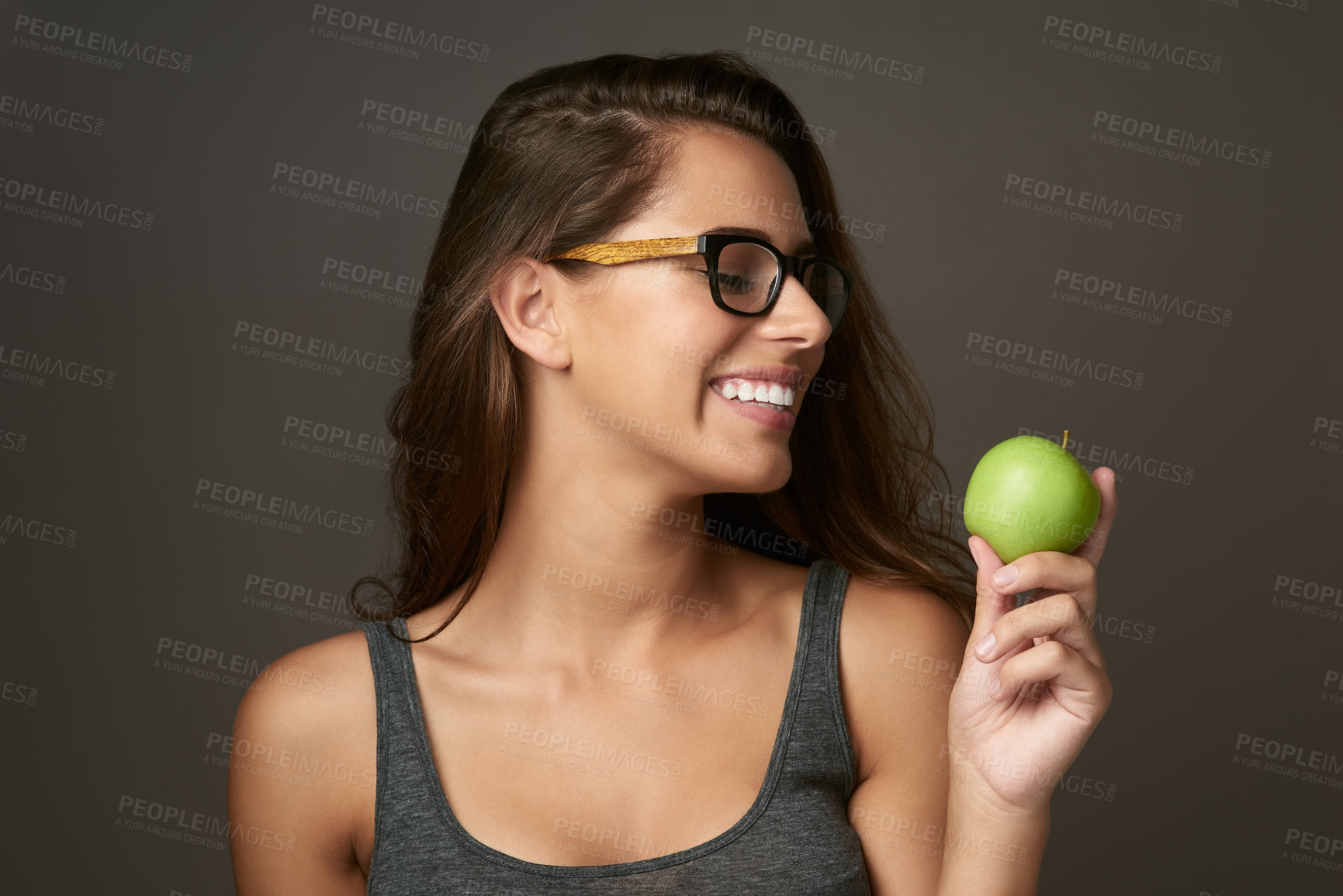 Buy stock photo Studio shot of a beautiful young woman looking at an apple against a brown background