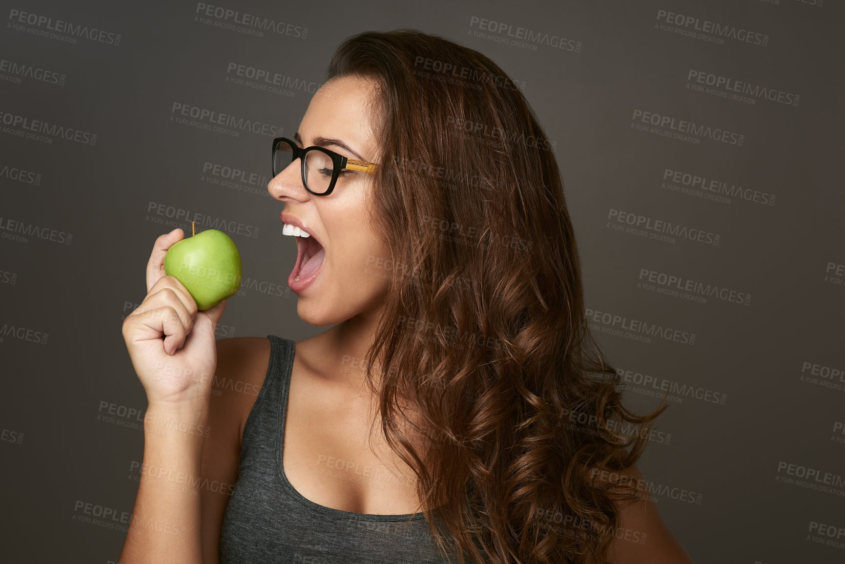 Buy stock photo Studio shot of a beautiful young woman about to bite an apple against a brown background