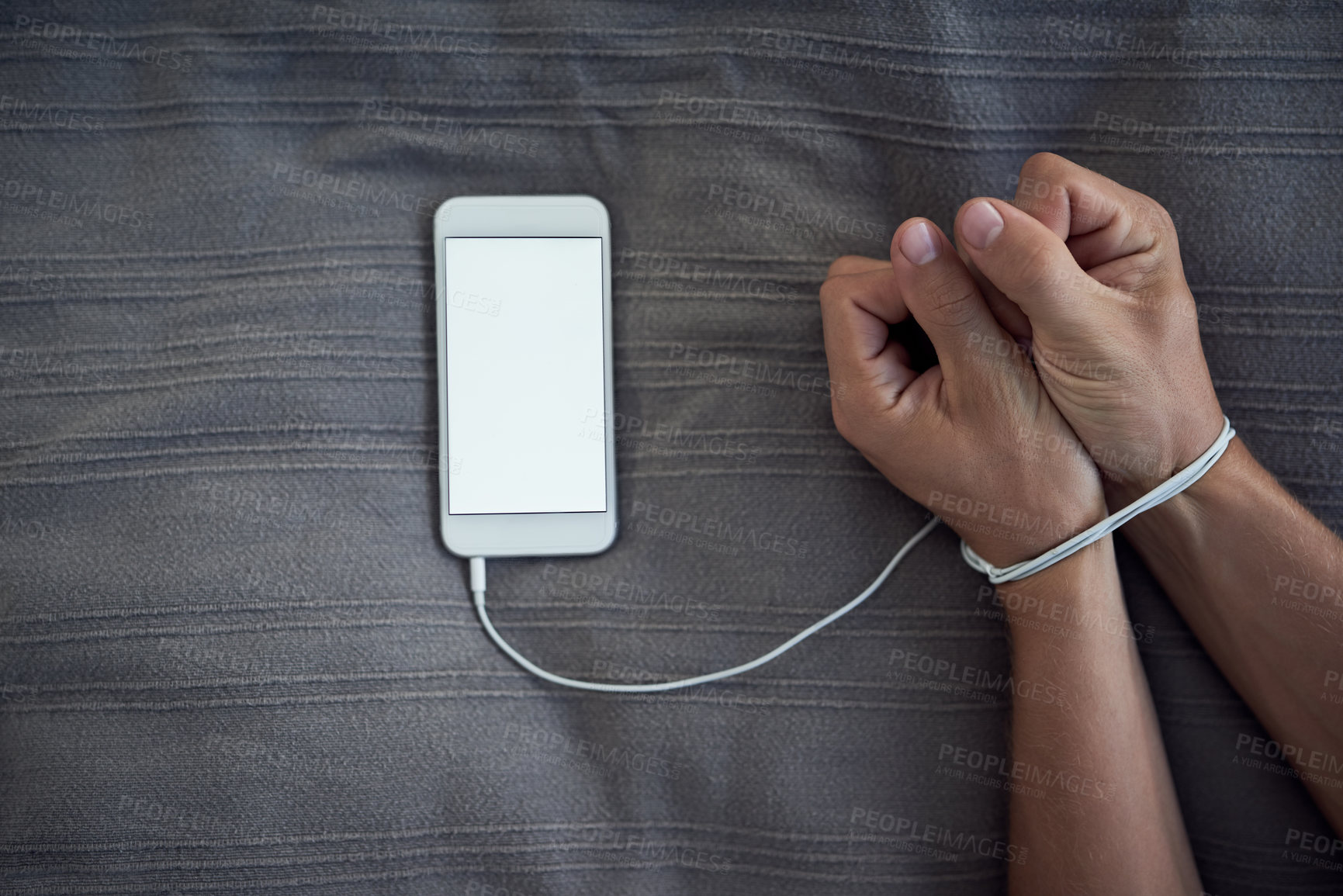 Buy stock photo Cropped shot of a unrecognizable person's hands bound by a cellphone charging cable