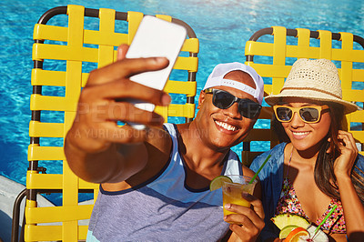 Buy stock photo High angle shot of an affectionate young couple taking selfies while enjoying a few drinks poolside