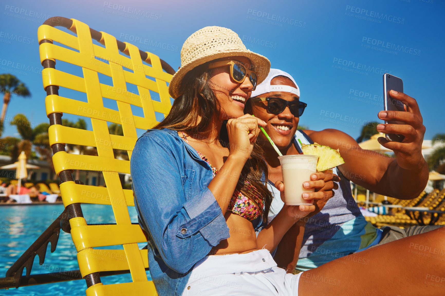 Buy stock photo Cropped shot of an affectionate young couple taking selfies while enjoying a few drinks poolside