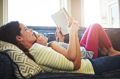 Buy stock photo Shot of a mother and her daughter reading a book together on the sofa at home