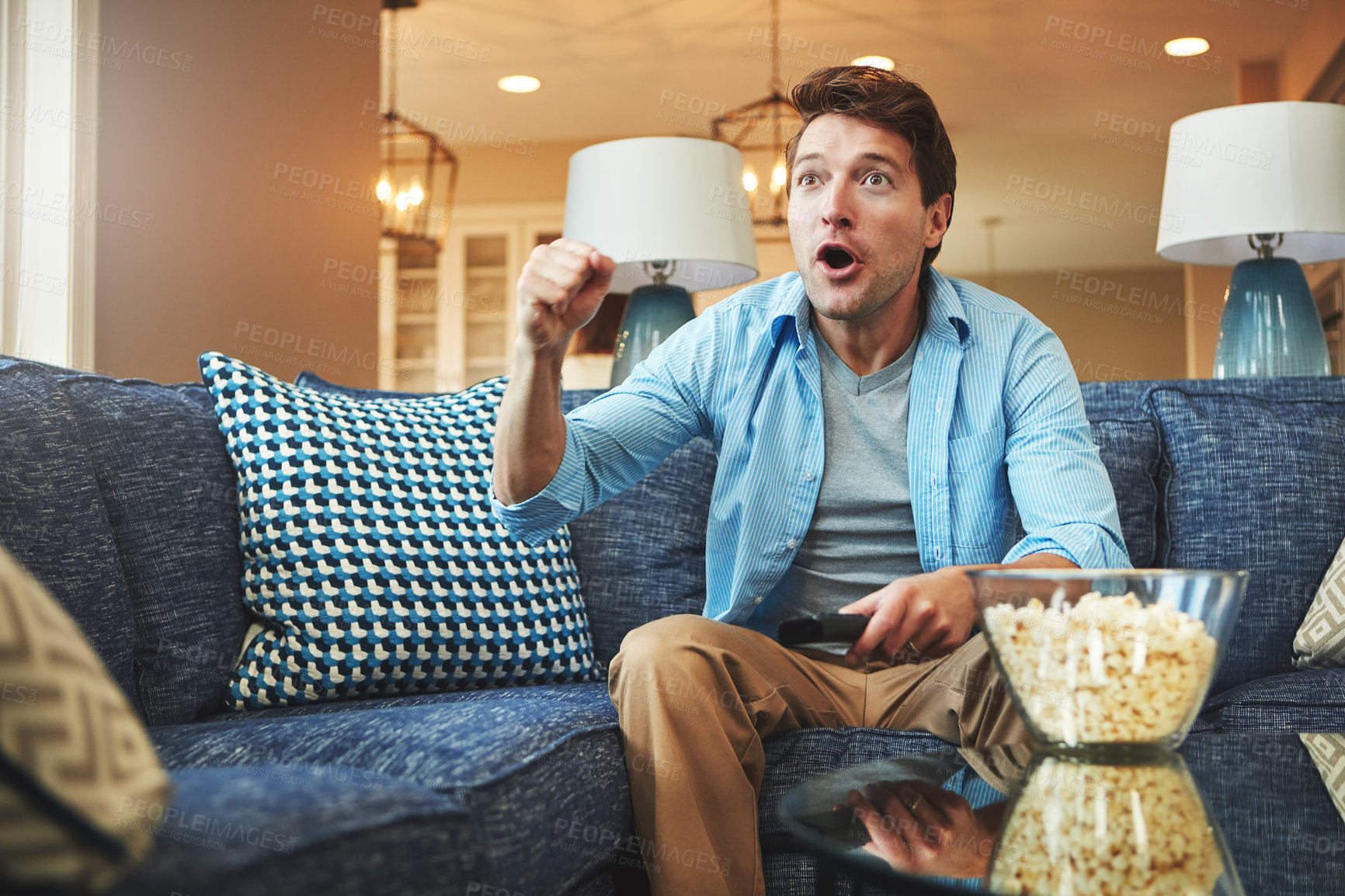 Buy stock photo Shot of a young man watching an exciting sports match on tv