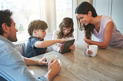 Buy stock photo Shot of a married couple and their young children playing with a tablet together in their kitchen