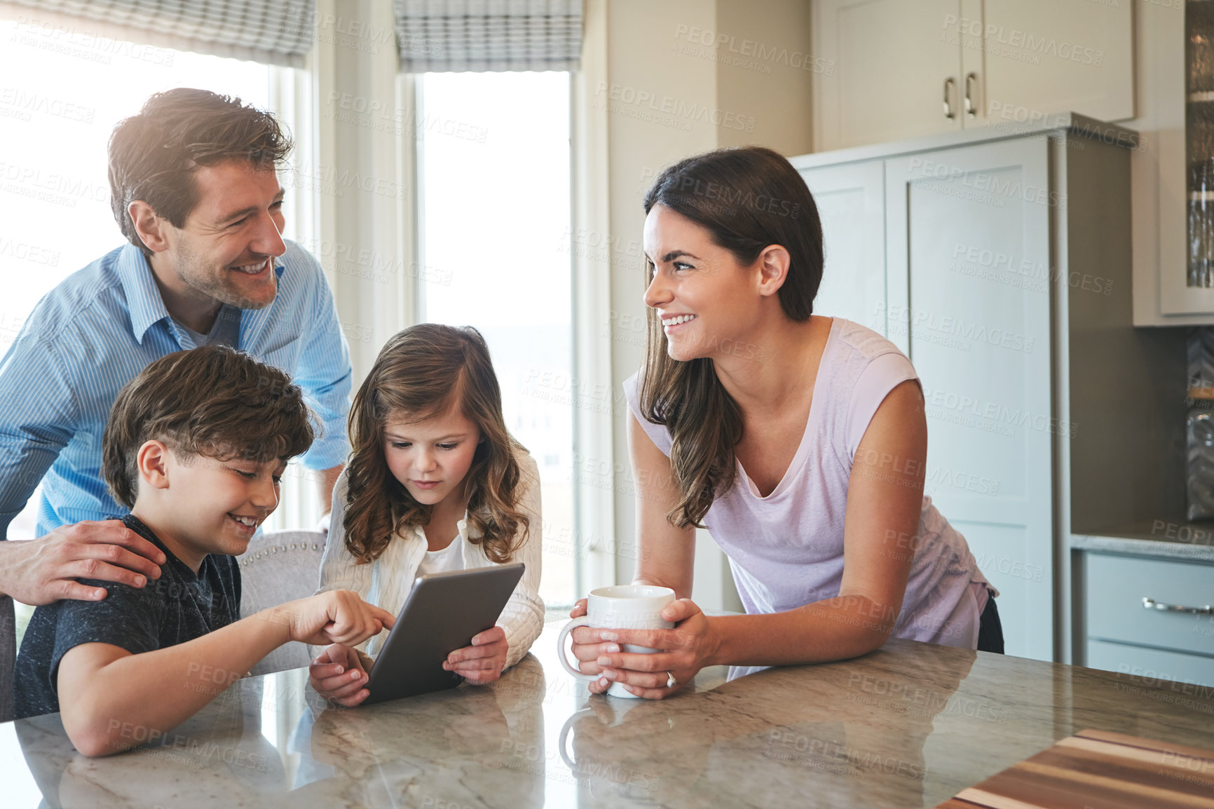 Buy stock photo Shot of a married couple and their young children playing with a tablet together in their kitchen