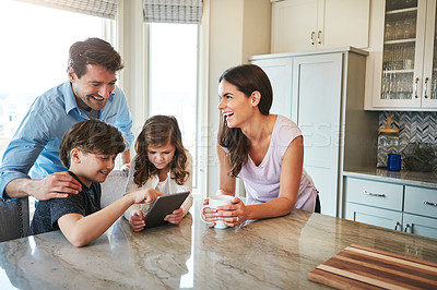 Buy stock photo Shot of a married couple and their young children playing with a tablet together in their kitchen