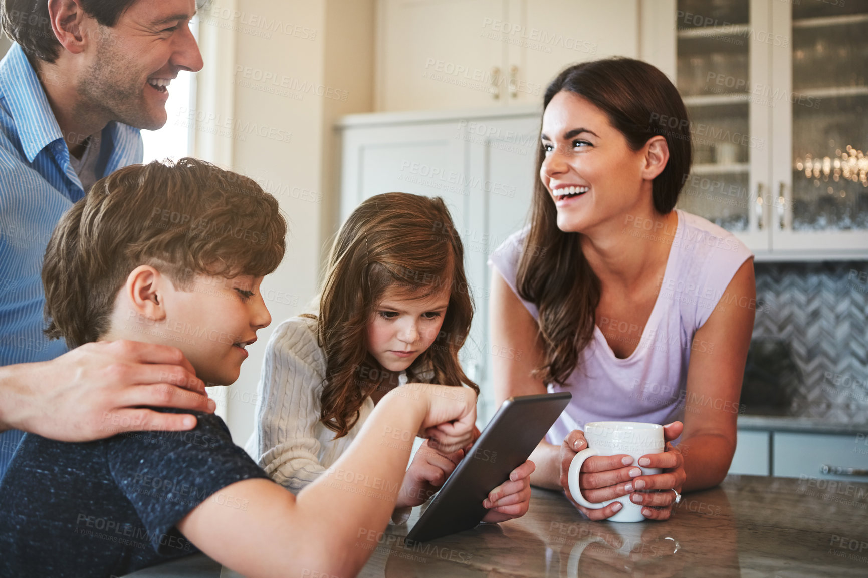 Buy stock photo Shot of a married couple and their young children playing with a tablet together in their kitchen