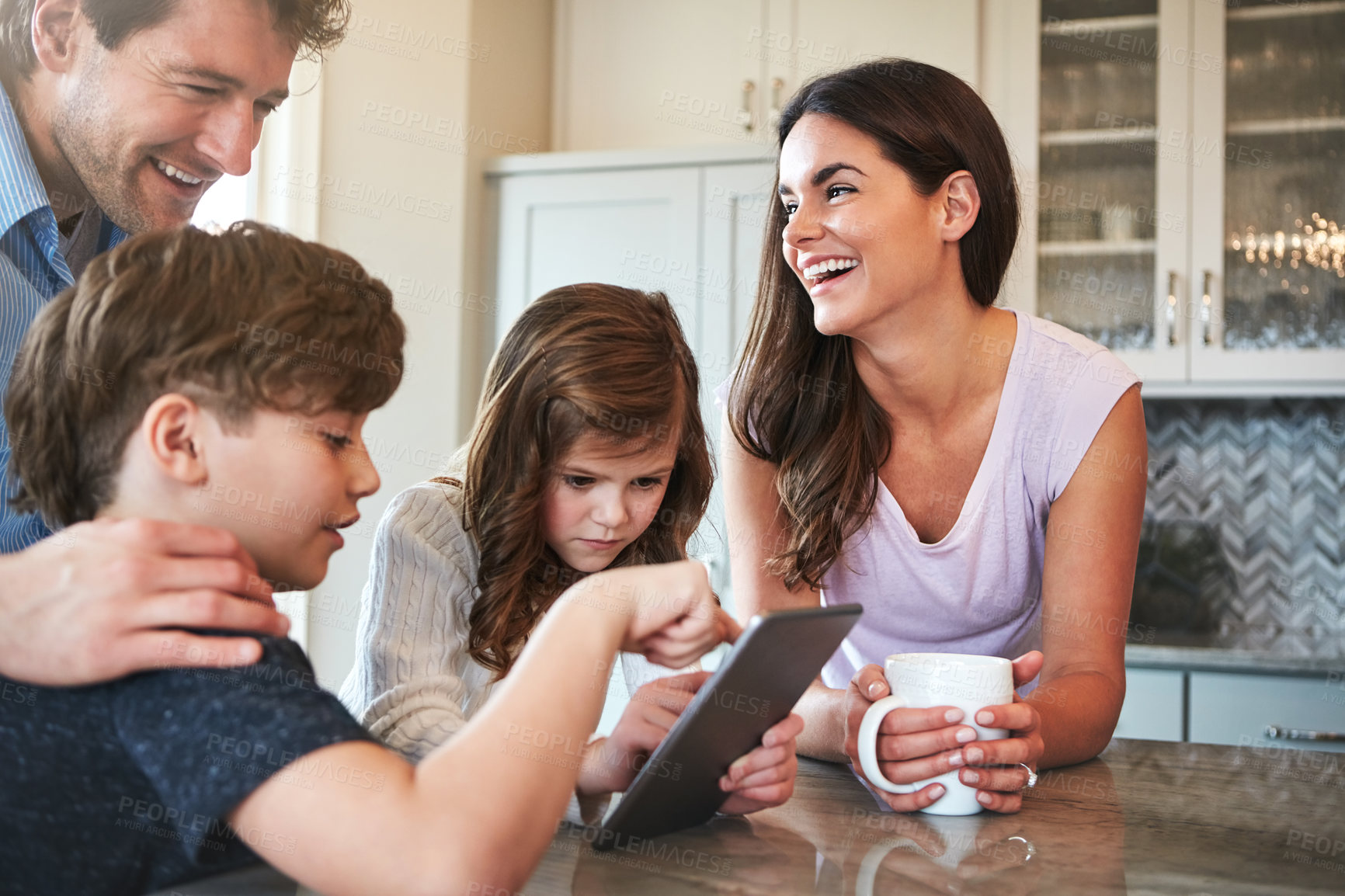 Buy stock photo Shot of a married couple and their young children playing with a tablet together in their kitchen