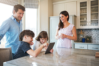 Buy stock photo Shot of a married couple and their young children playing with a tablet together in their kitchen