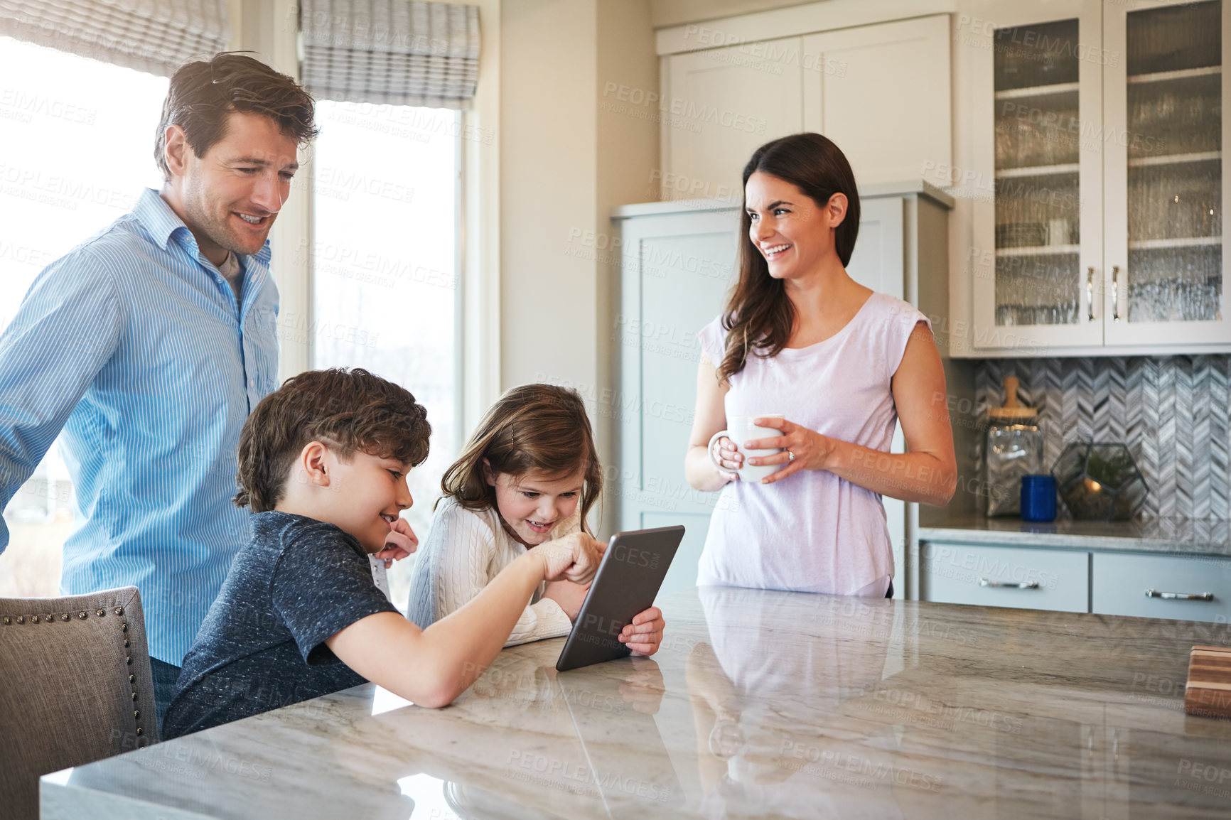 Buy stock photo Shot of a married couple and their young children playing with a tablet together in their kitchen