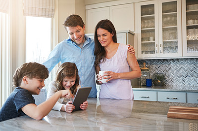 Buy stock photo Shot of a married couple and their young children playing with a tablet together in their kitchen