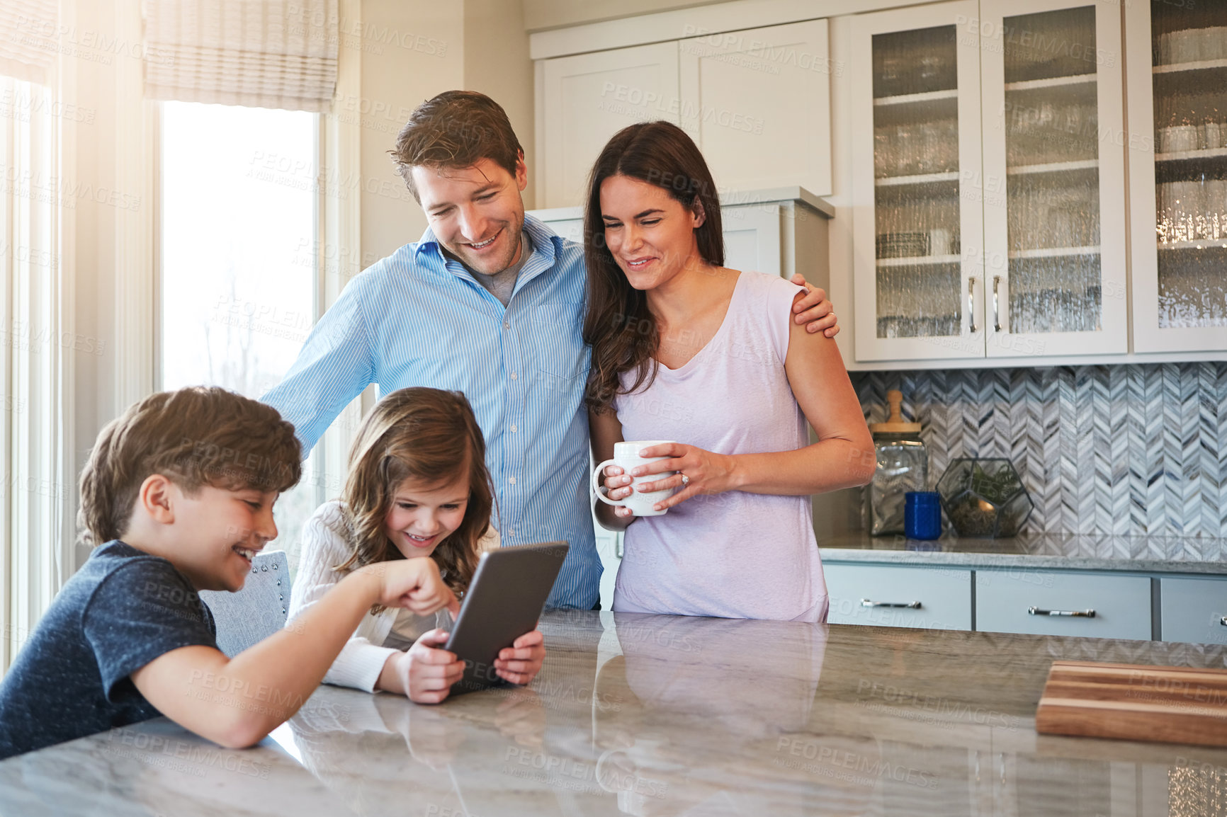 Buy stock photo Shot of a married couple and their young children playing with a tablet together in their kitchen