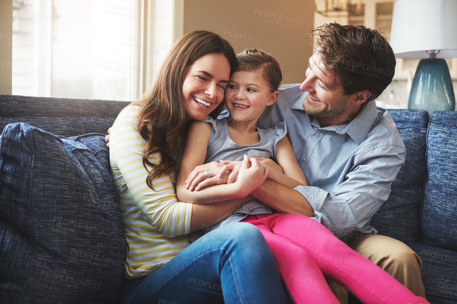 Buy stock photo Hugging, happy and child with parents on sofa in home relaxing with care, fun and love together. Laughing, bonding and girl kid embracing with mother and father in living room at family house.