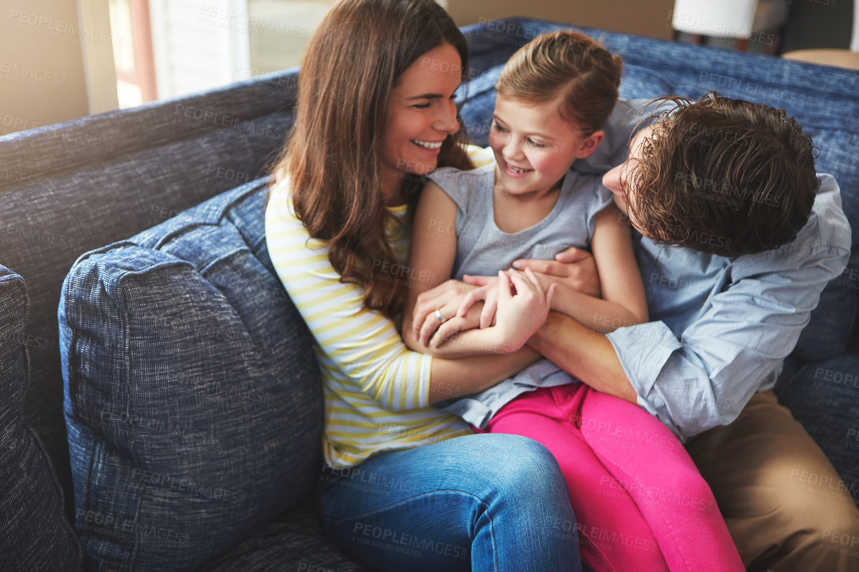 Buy stock photo Tickling, happy and child with parents on sofa in home relaxing with care, fun and love together. Laughing, smile and girl kid play and bonding with mother and father in living room at family house.