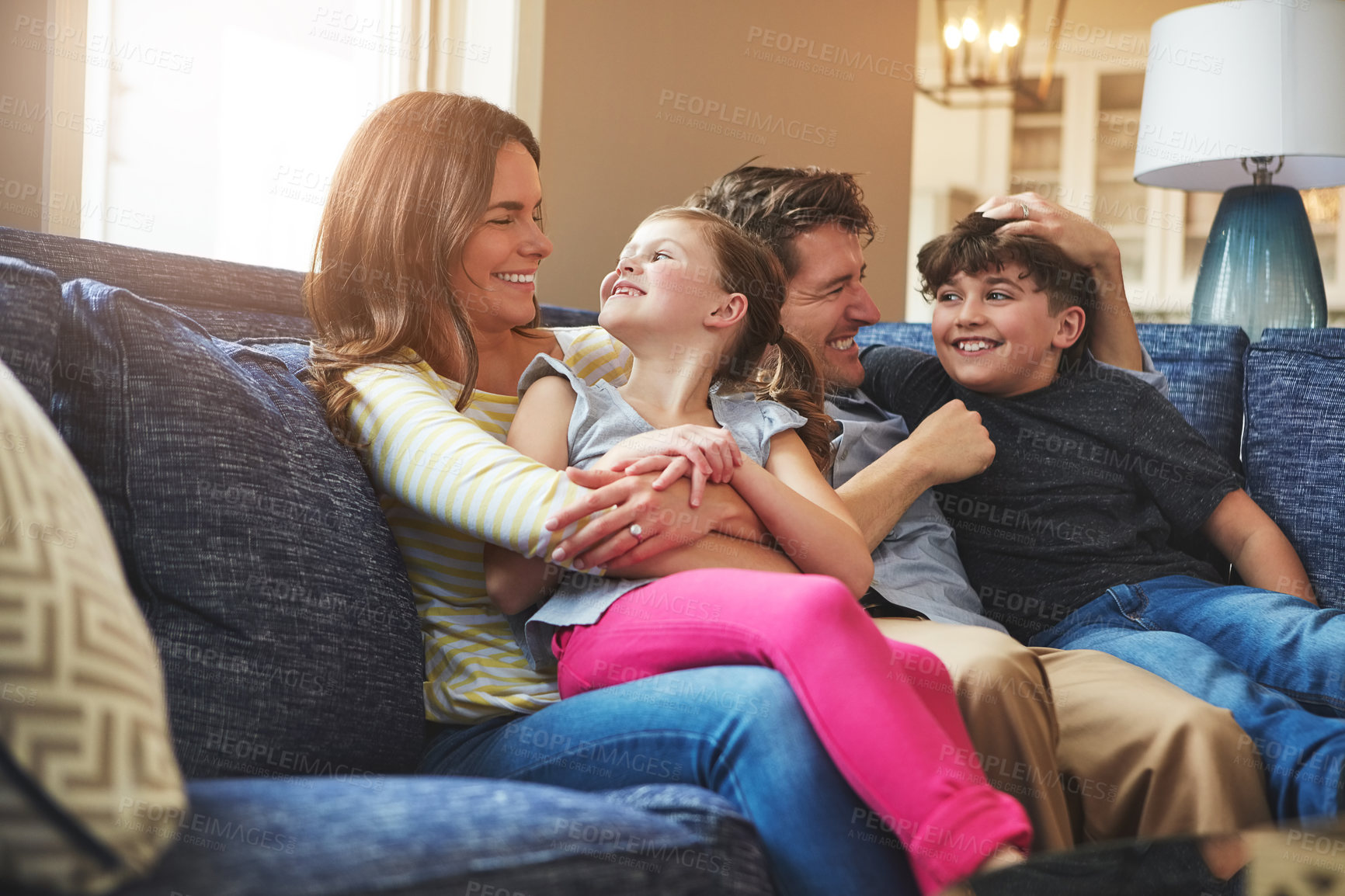 Buy stock photo Hugging, happy and children with parents on sofa in home relaxing with care, fun and love together. Laughing, bonding and kids embracing with mother and father in living room at family house.