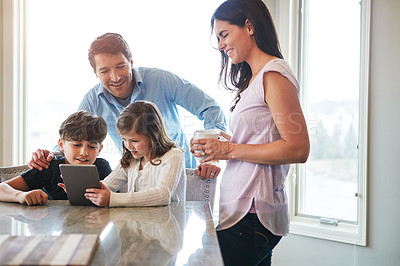 Buy stock photo Shot of a married couple and their young children playing with a tablet together in their kitchen