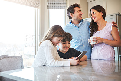 Buy stock photo Shot of a married couple and their young children playing with a tablet together in their kitchen