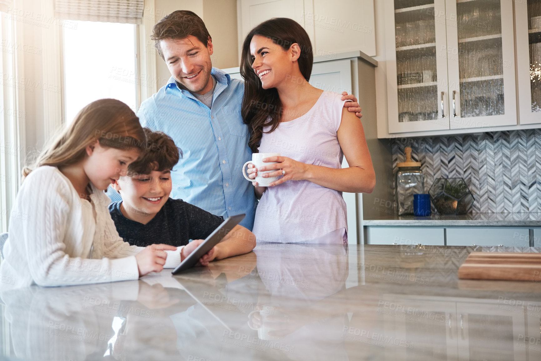 Buy stock photo Shot of a married couple and their young children playing with a tablet together in their kitchen