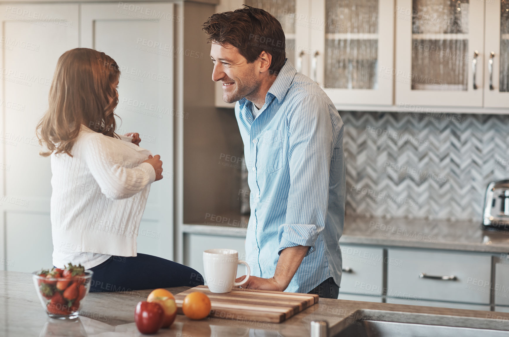 Buy stock photo Shot of a happy little girl chatting with her father while sitting on the kitchen counter at home