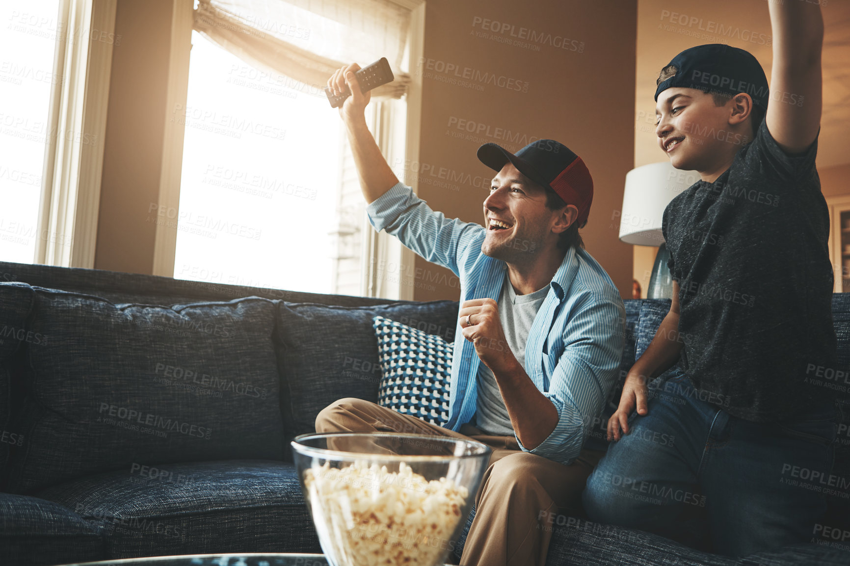 Buy stock photo Television, child and man with celebration on sofa for streaming, network and watching together. Dad, son and popcorn with tv remote at home for success, bonding and live broadcast of sports match