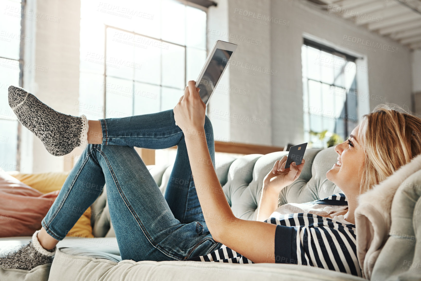 Buy stock photo Shot of a young woman relaxing on the sofa and using a credit card with a digital tablet