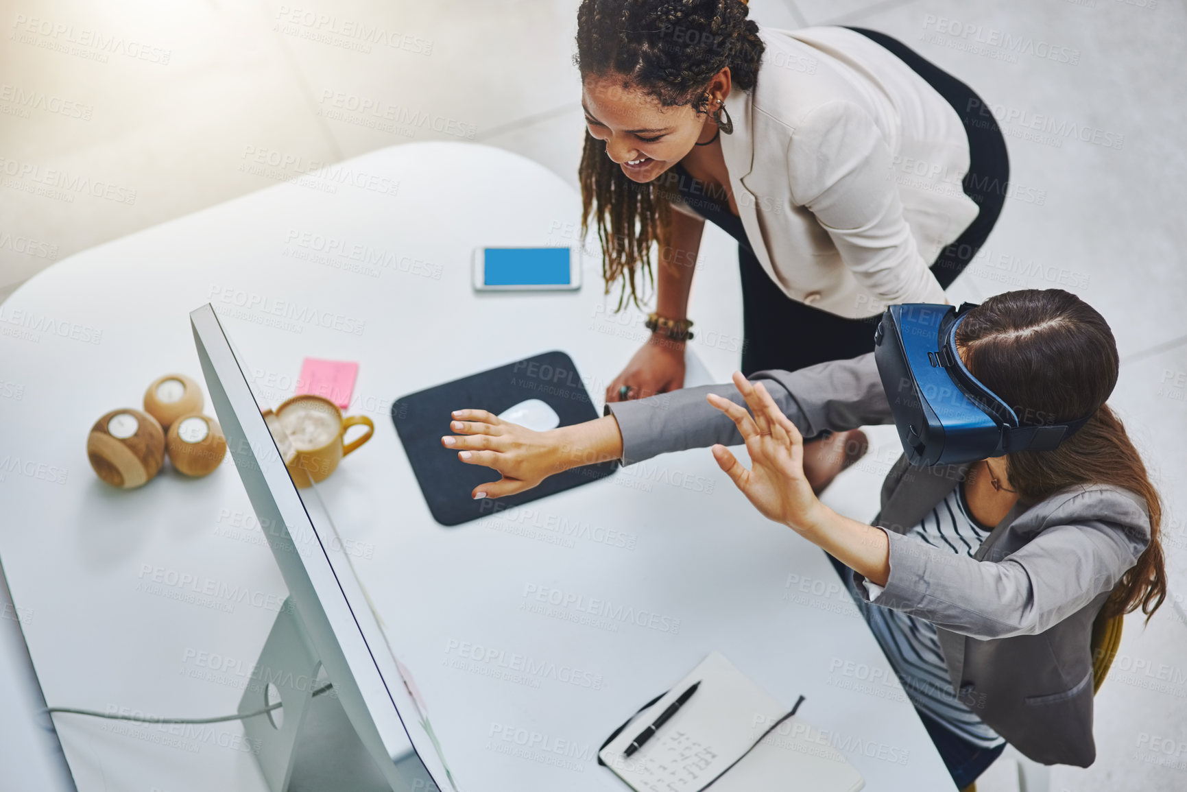 Buy stock photo High angle shot of a young businesswoman using a VR headset while being assisted by a female colleague