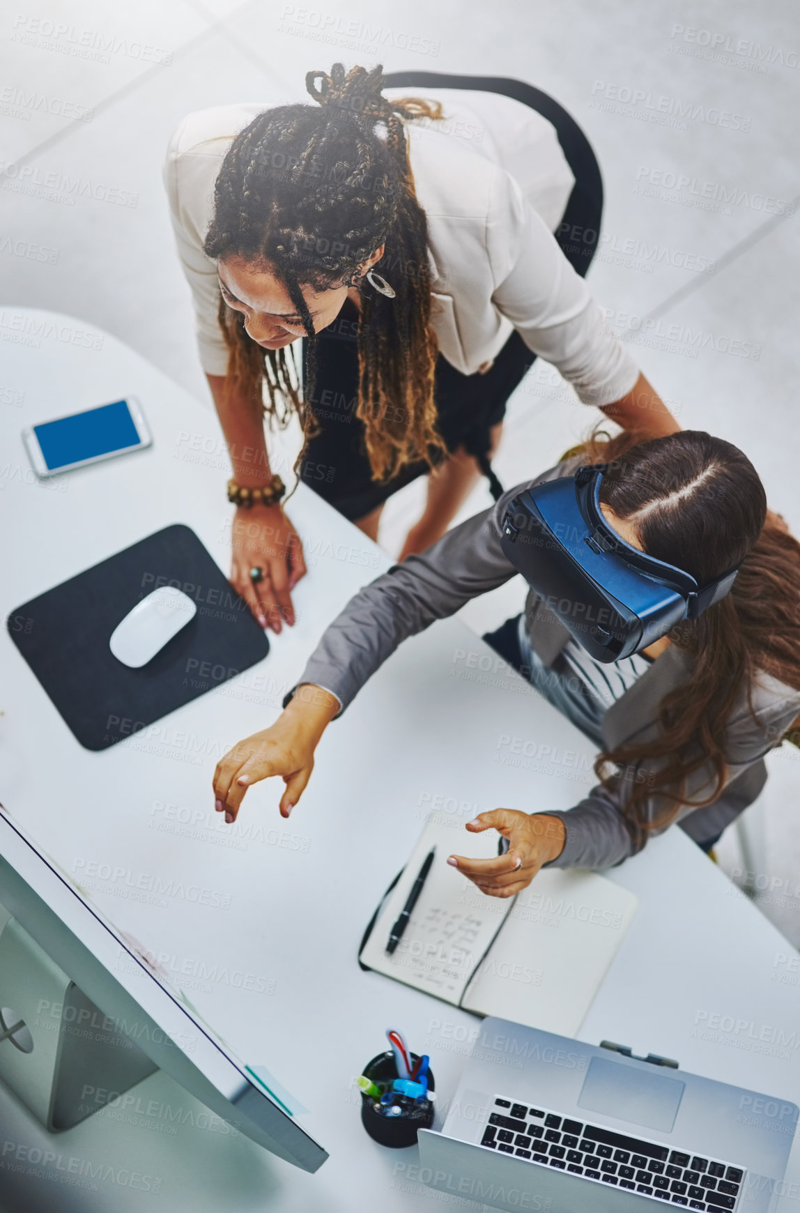 Buy stock photo High angle shot of a young businesswoman using a VR headset while being assisted by a female colleague