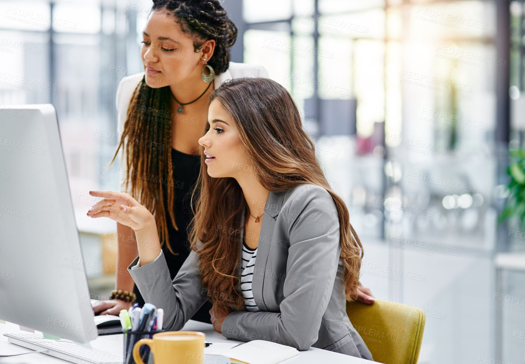 Buy stock photo Cropped shot of two attractive young businesswomen working at a desk in their office