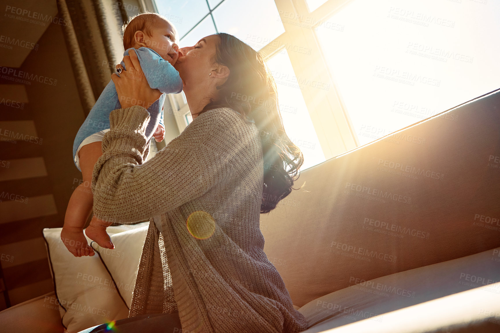 Buy stock photo Baby, mother and kiss on cheek in living room on sofa with love for relationship with new born, care. Embrace, sunshine and light in house on couch with playing, joy and happy woman with child.