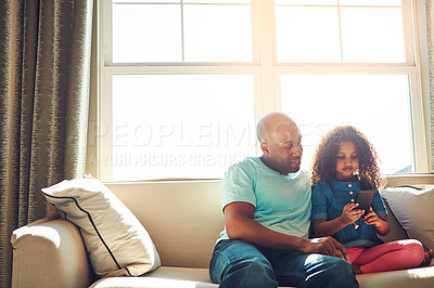 Buy stock photo Shot of a happy father watching his little girl while she plays with his smartphone on the couch at home